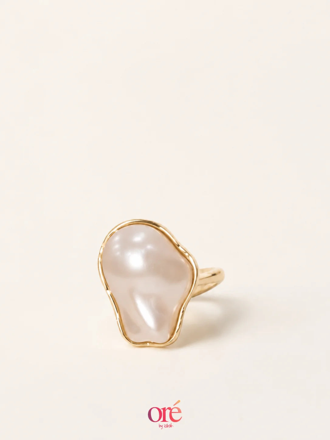 A gold ring featuring an organic, irregularly shaped white pearl, photographed on a clean, solid off-white background with a brand watermark at the bottom.