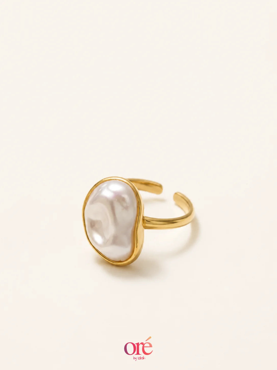 A gold adjustable ring featuring a large, irregularly shaped white pearl bezel-set in a polished gold-tone band, photographed on a warm off-white background with the 'ore by ore' logo at the bottom.