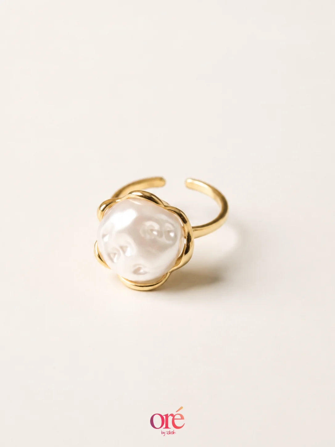 A gold-plated open ring featuring a large, polished white pearl cabochon, photographed on a clean, solid off-white background with a soft shadow.