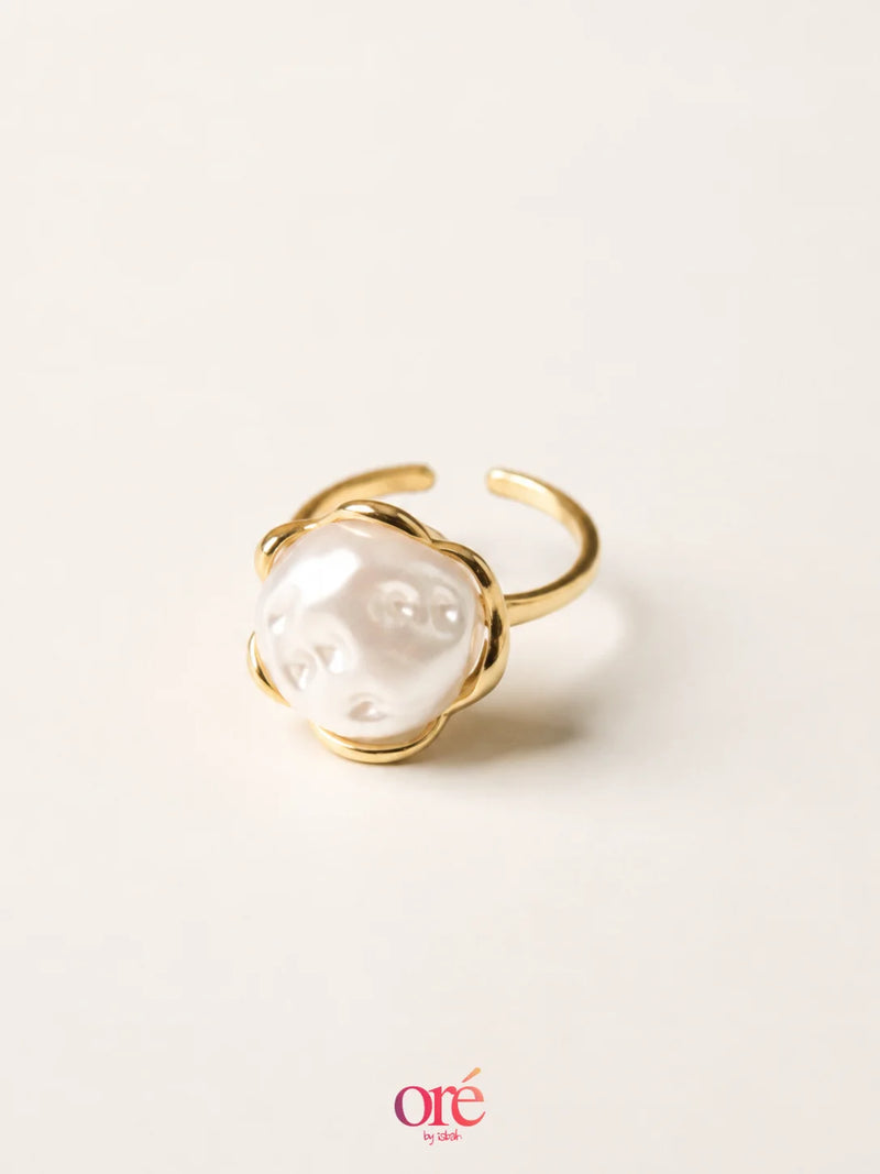 A gold-plated open ring featuring a large, polished white pearl cabochon, photographed on a clean, solid off-white background with a soft shadow.