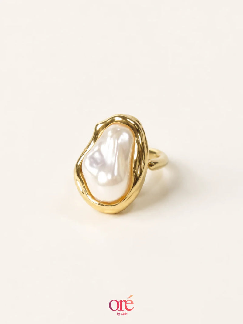 A gold-plated open ring featuring a large, polished white pearl cabochon, photographed on a clean, solid off-white background with a soft shadow.

