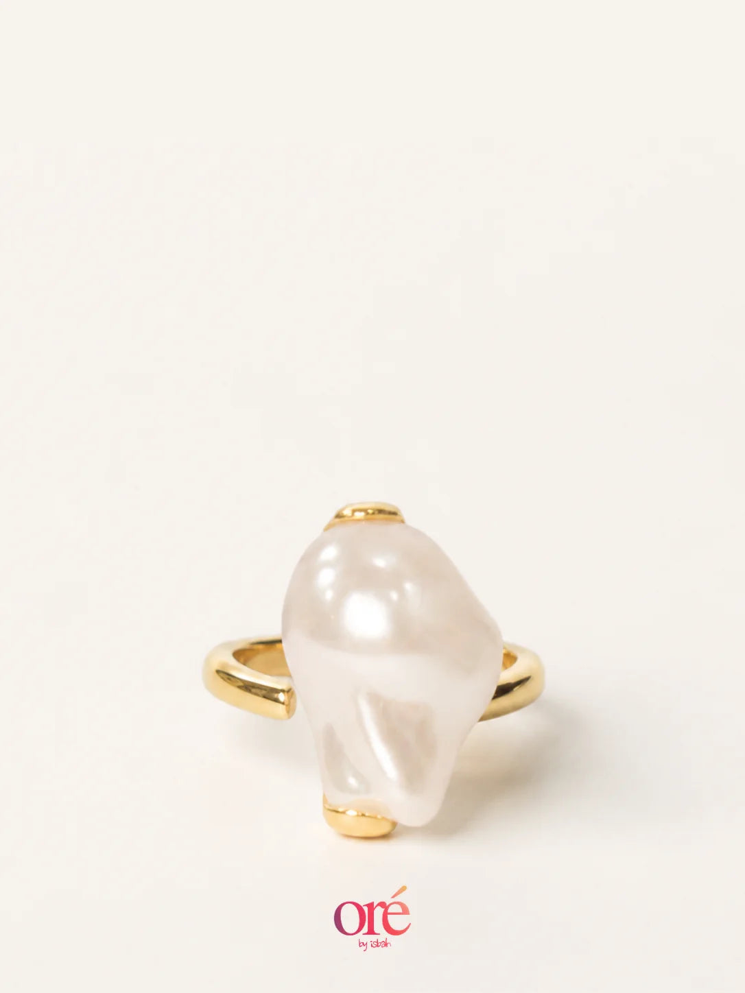 A gold ring featuring a large, irregular white pearl-like stone, photographed on a clean off-white background with an 'ore by ora' logo at the bottom.