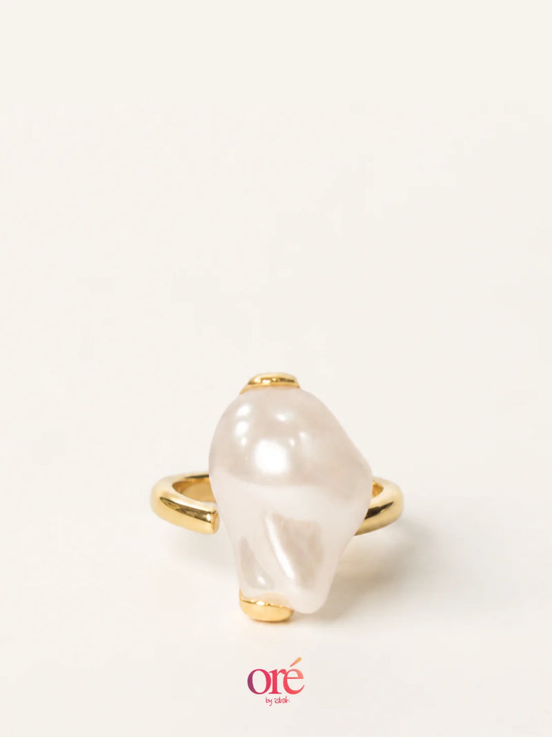 A gold ring featuring a large, irregular white pearl-like stone, photographed on a clean off-white background with an 'ore by ora' logo at the bottom.